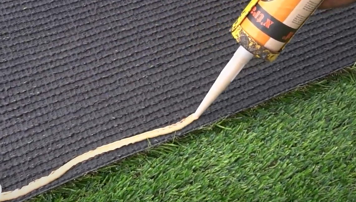 A worker using silicone glue applied directly to the floor surface to hold the turf.