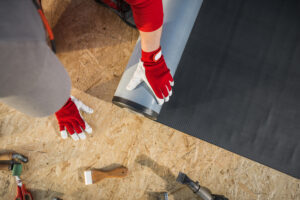 A worker installing a carpet underlay on the flooring, surrounded by various tools on a wooden surface.