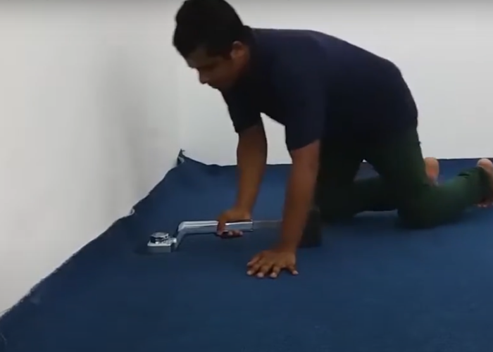 Professional installer fitting blue office carpet using a carpet stretcher tool during installation.