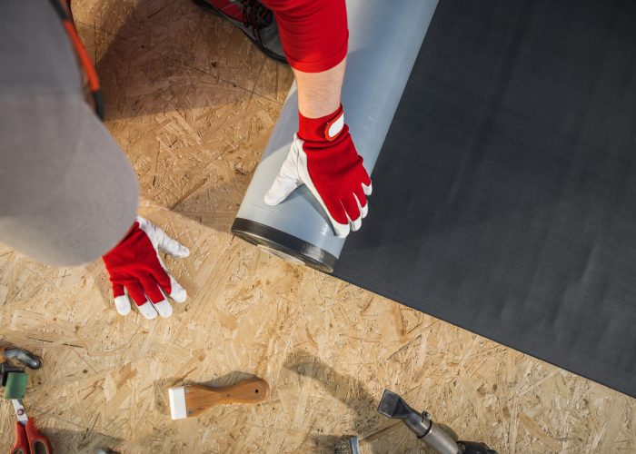 A worker installing a carpet underlay on the flooring, surrounded by various tools on a wooden surface.